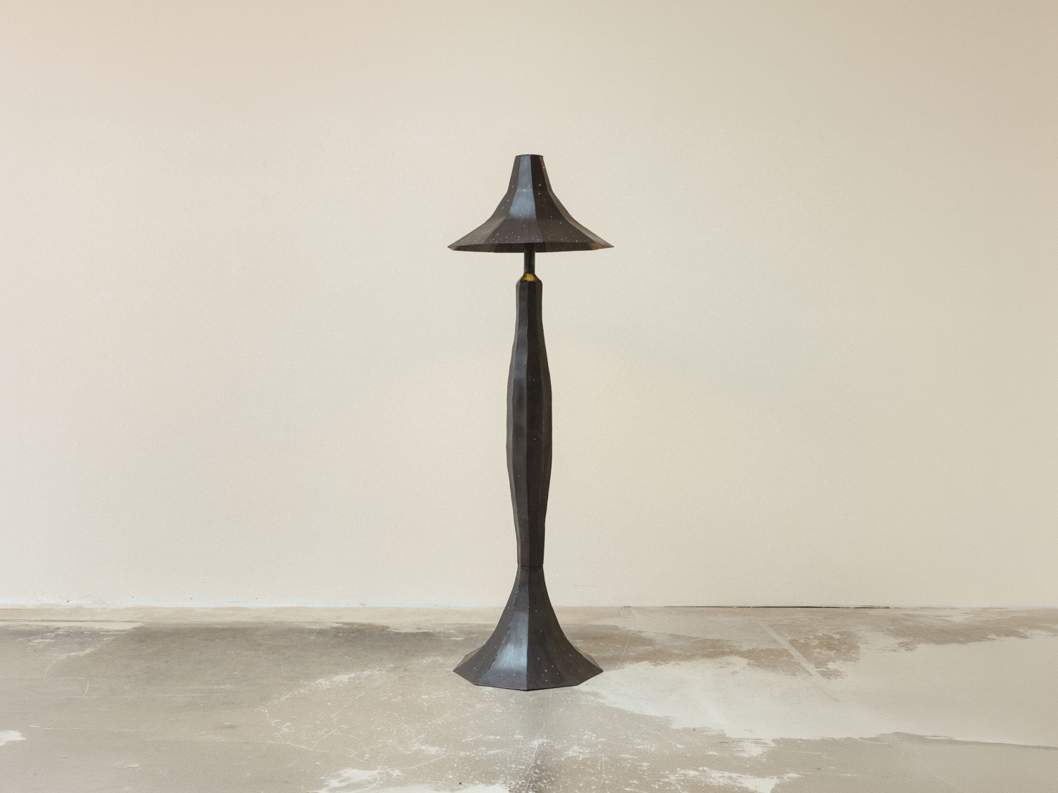 Dark patinated metal floor lamp with a sculptural faceted body and flared bell shade pricked with pinholes, standing on concrete — Studio Kuhlmann Dew Darling