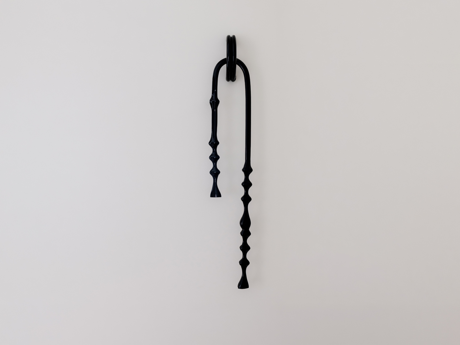 Black knotted wall light shaped like a looped strap over a ring, two tapered beaded arms of differing lengths dangling down a pale wall — Kimy Gringoire OTAGEP EARRING LIGHT