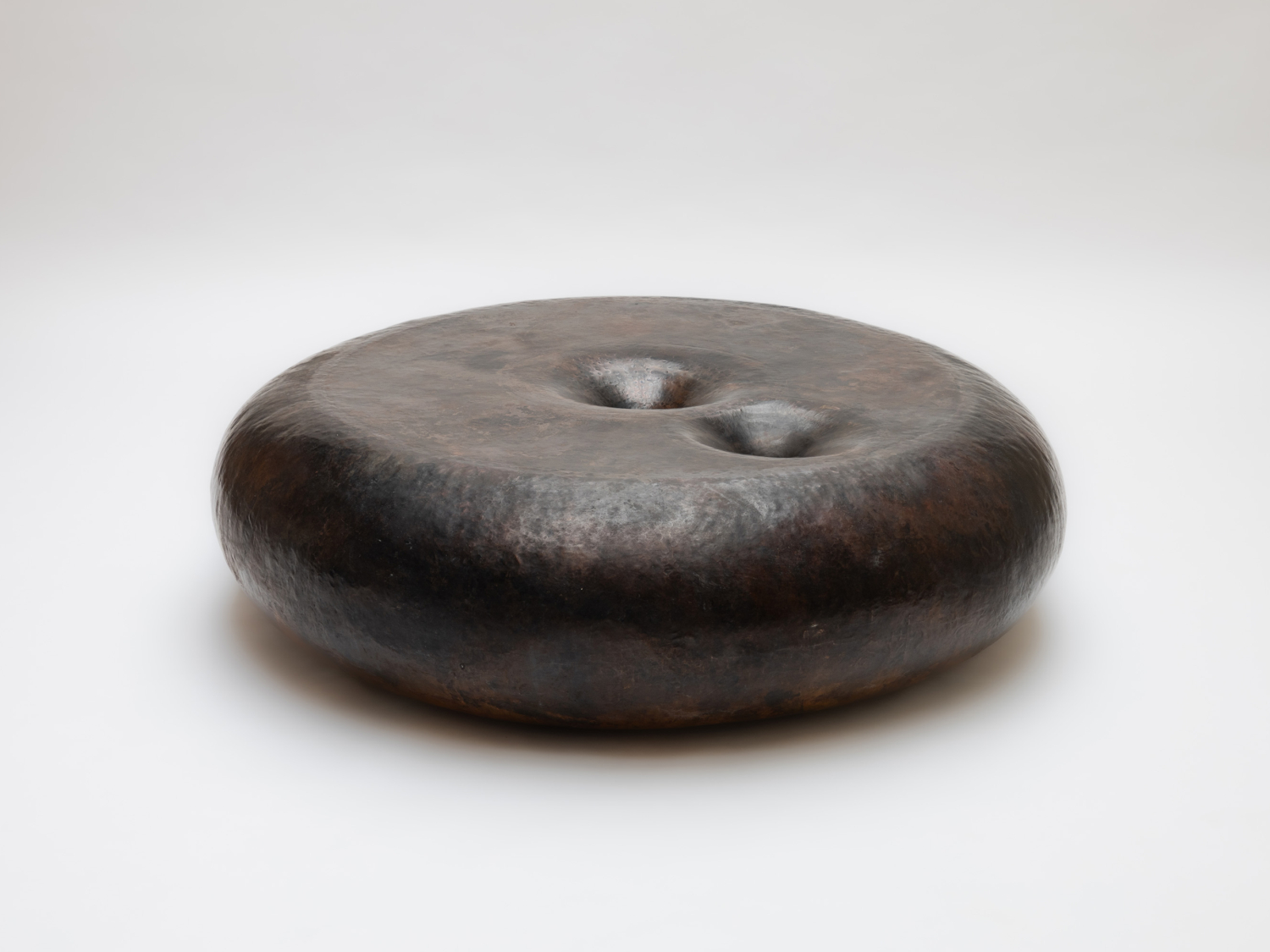 Rounded cast bronze disc sculpture with a dark mottled patina and two dimpled hollows on its domed top — Brian Thoreen Untitled Double Vortics