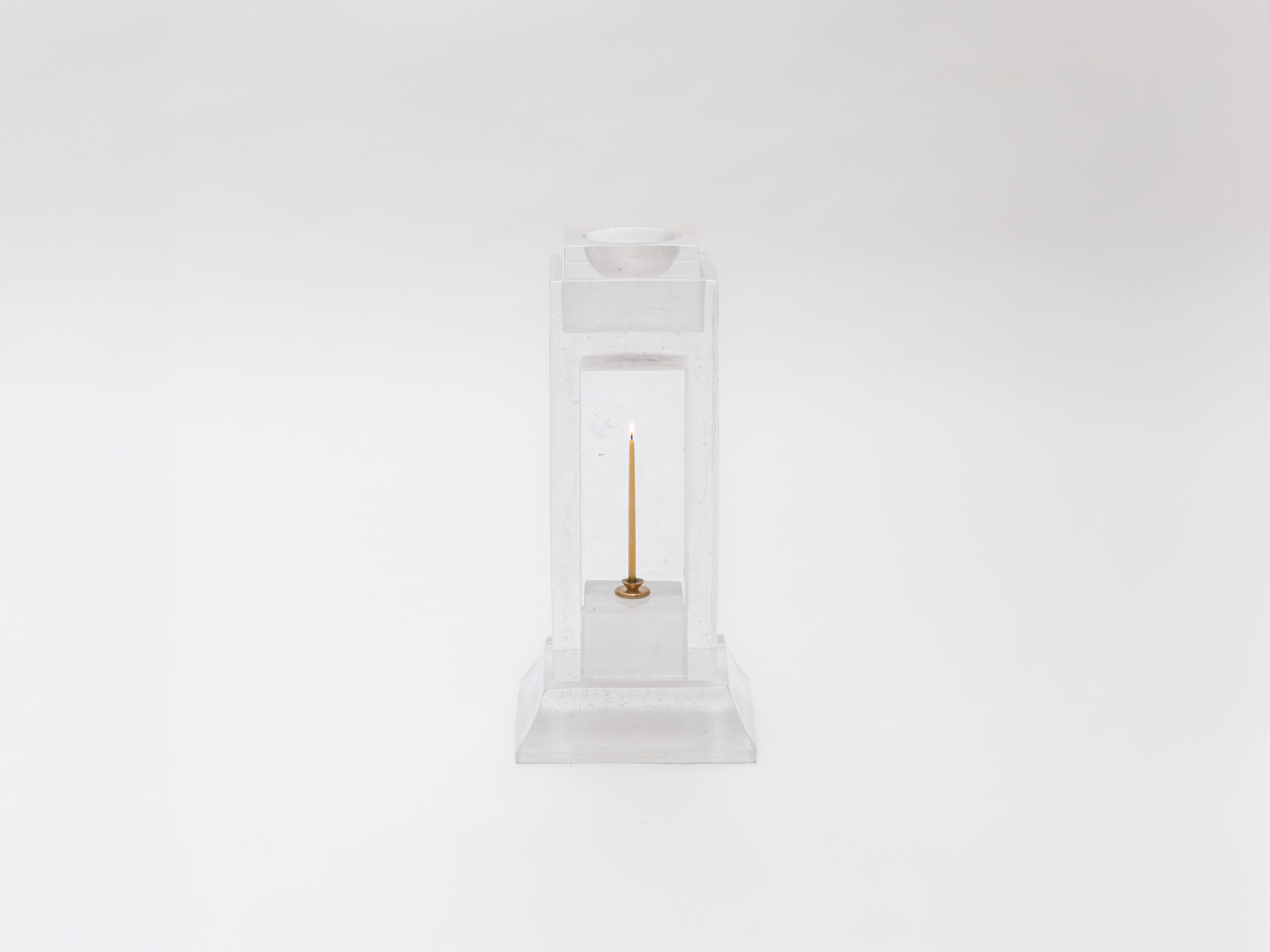 Clear cast-glass smoking table in stacked blocks framing a lit taper candle on a brass holder, on a stepped base — Emily Thurman Stacks Smoking Table