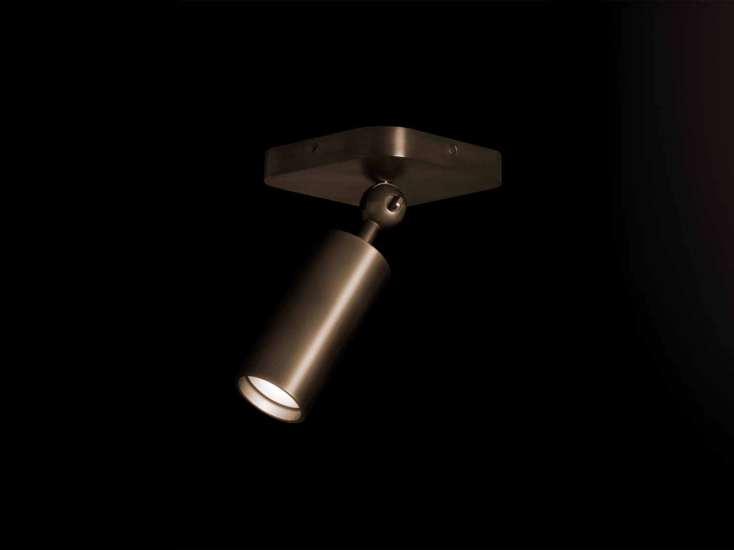 Ceiling-mounted downlight with square canopy and adjustable brushed-bronze cylindrical spot, illuminated lens angled down — Apparatus Studio Cylinder Downlight