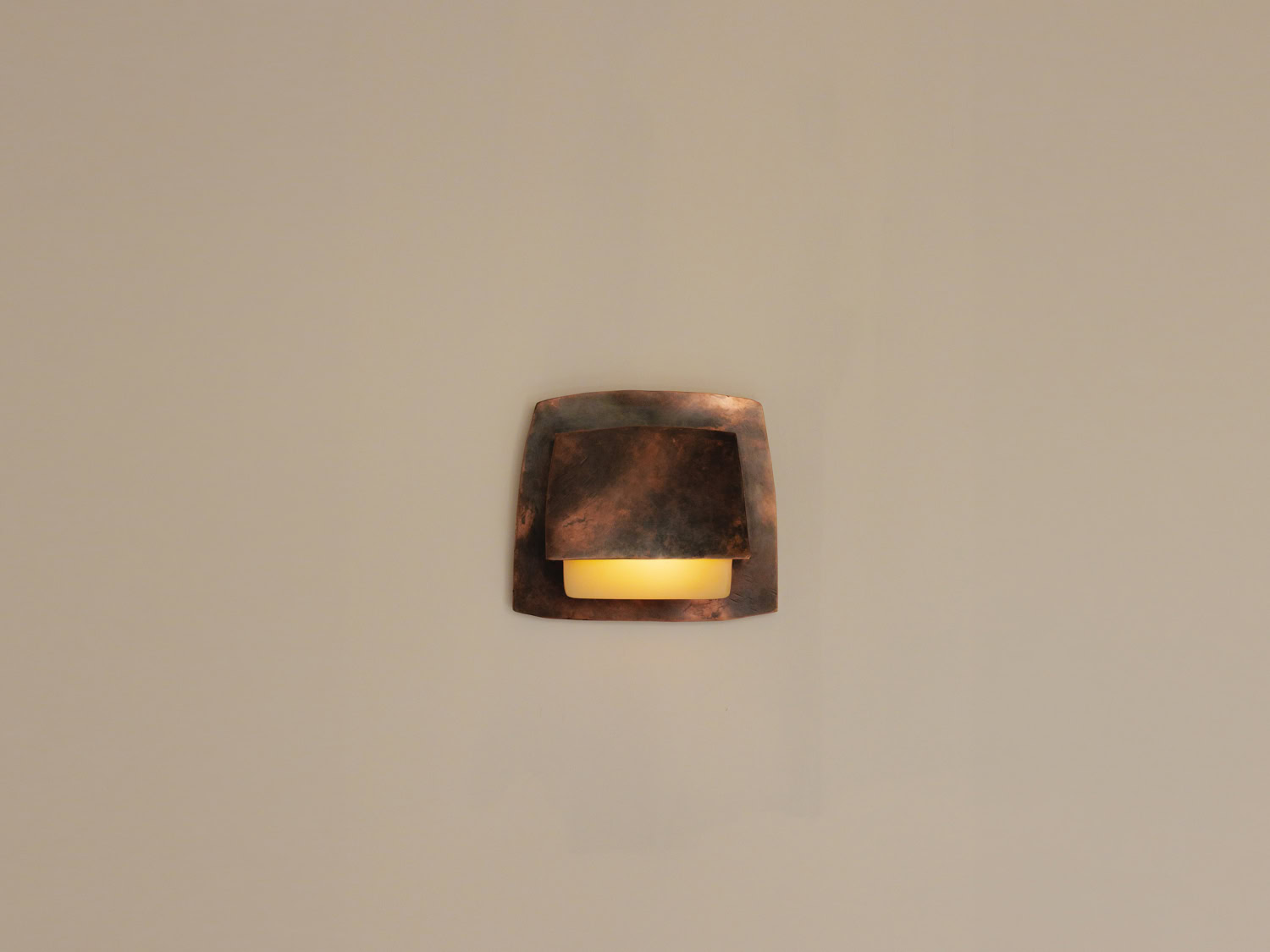 Small mottled copper wall sconce, two overlapping square plates shielding a softly glowing amber cylindrical diffuser — Nick Valentijn Wall Lamp